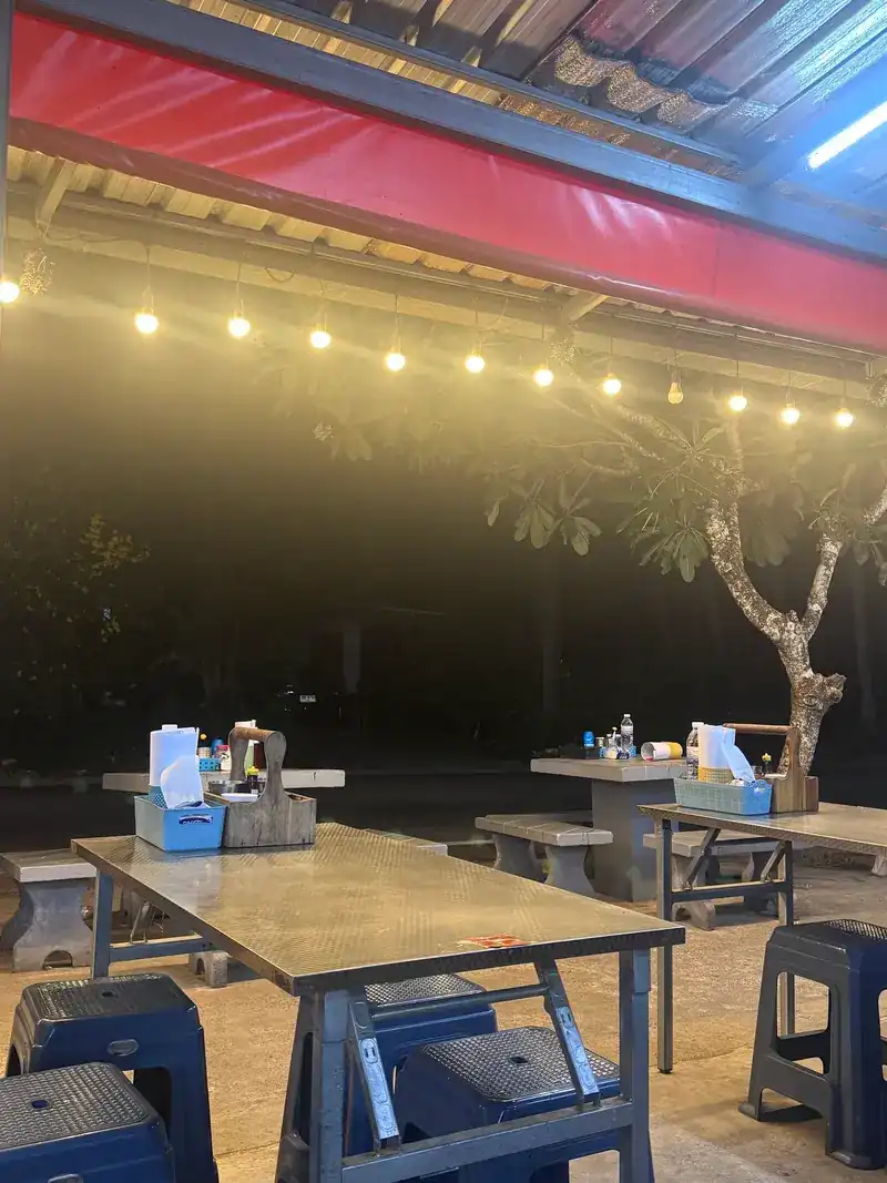 Outdoor tables and stools under the red awning, lit by a row of bulbs at night