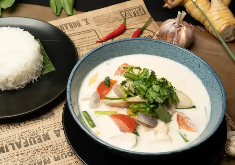 A bowl of tom kha coconut soup with jasmine rice beside it