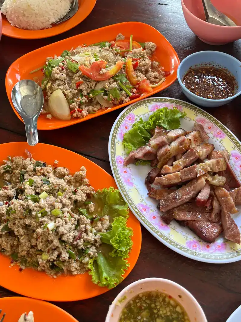 Two plates of larb, sliced grilled beef with lettuce and a bowl of dipping sauce