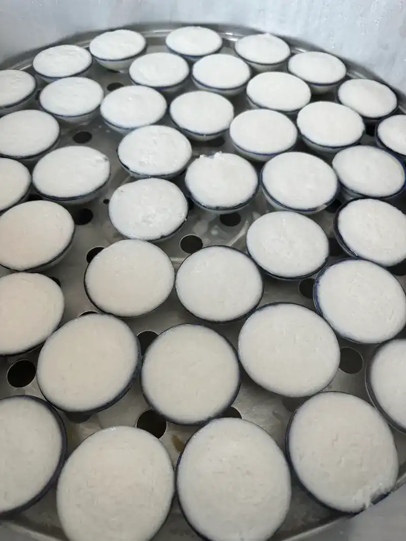 Rows of khanom thuai coconut cups in a steamer