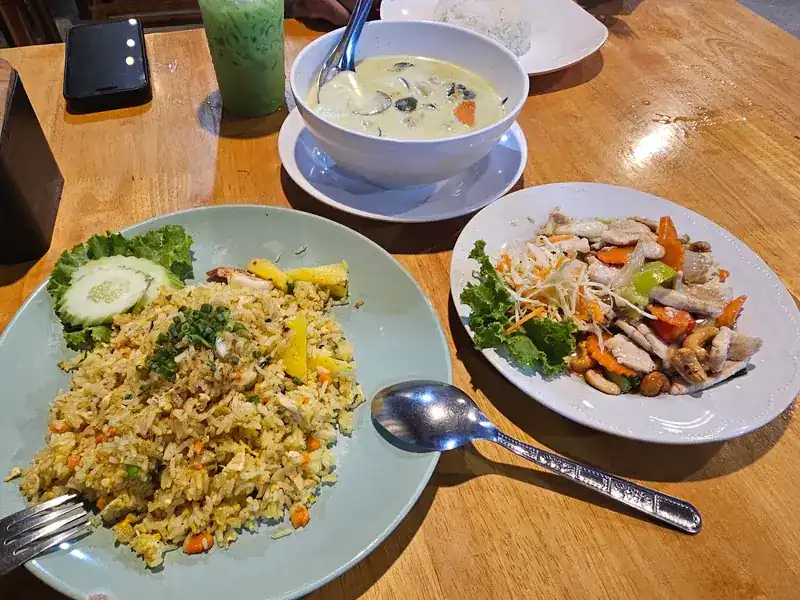 Fried rice, a bowl of green curry and stir-fried chicken with cashew nuts on a wooden table