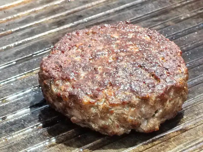 A thick burger patty searing on a ridged grill