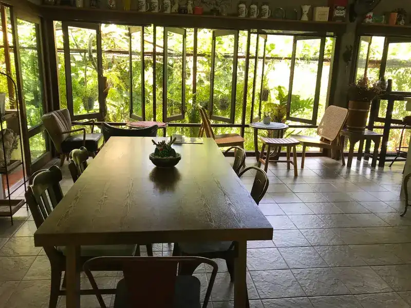 A long wooden table in a room of folding glass windows, with the garden outside