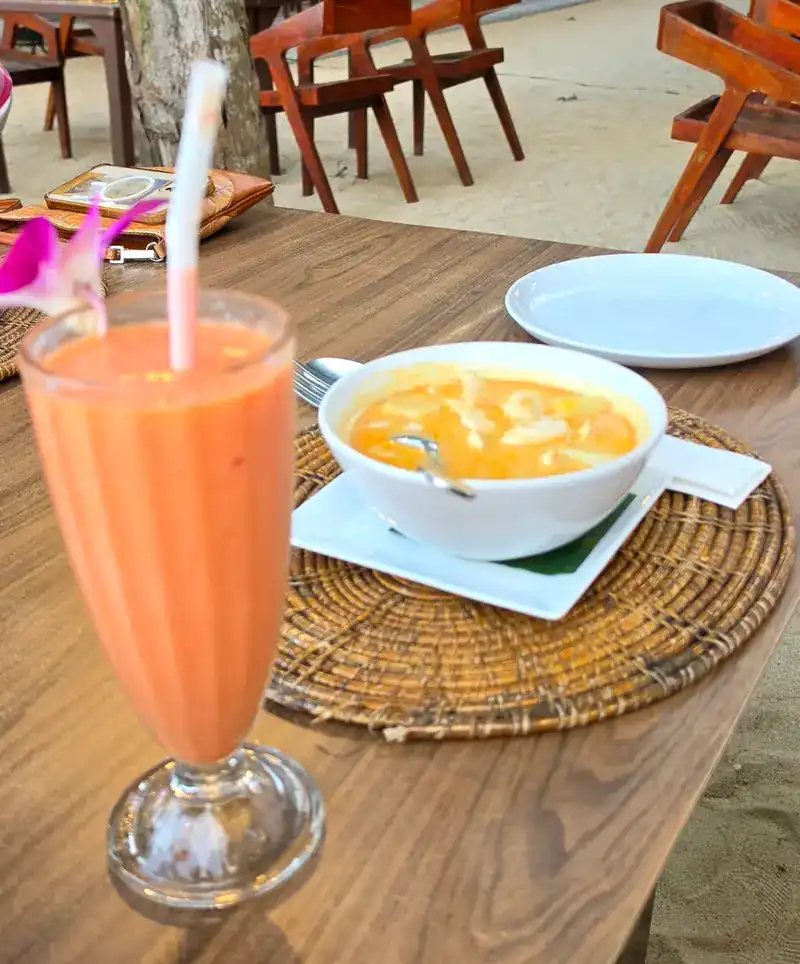 A tall orange blended drink and a small bowl on a woven place mat