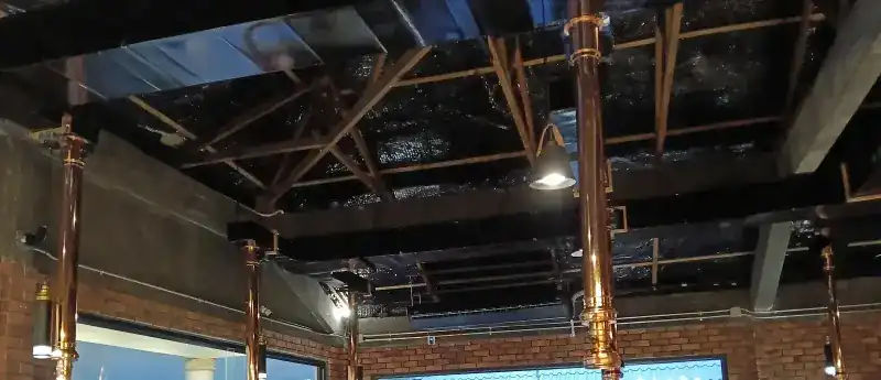 The dining room ceiling: black beams, a pendant lamp and copper smoke ducts above the tables, brick walls below