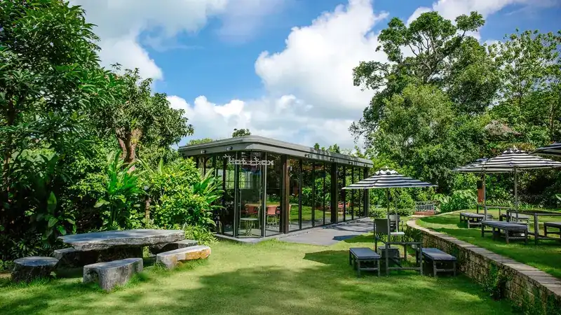 The Hot Box glass pavilion in a tropical garden with stone benches and umbrellas