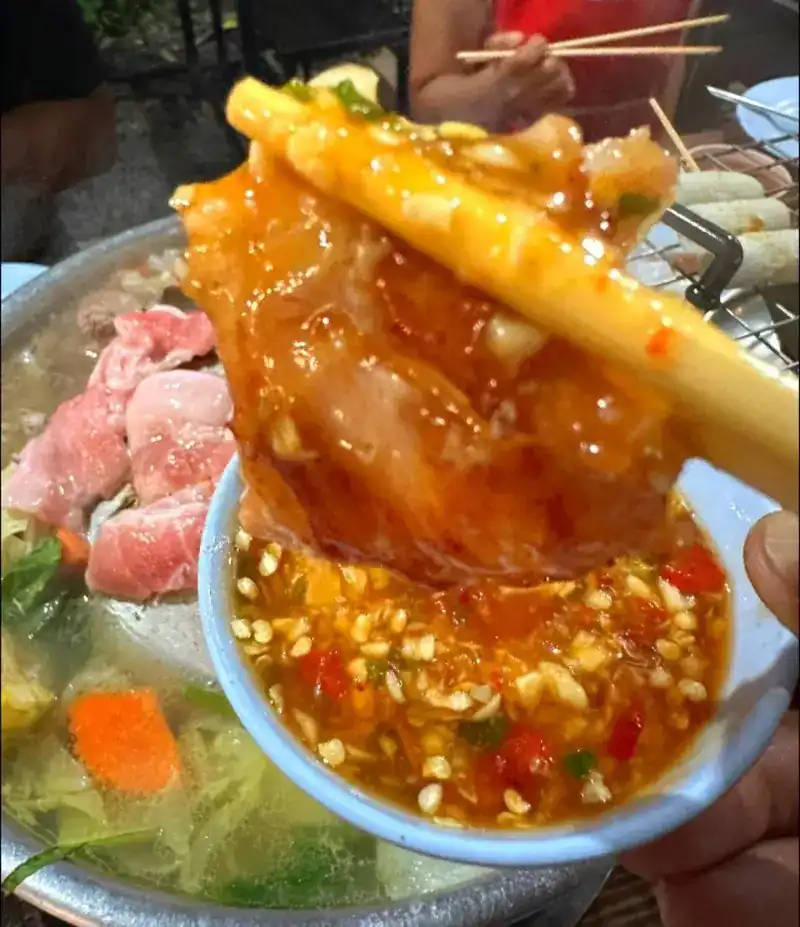 A piece of pork lifted from the pan and dipped in chilli sauce