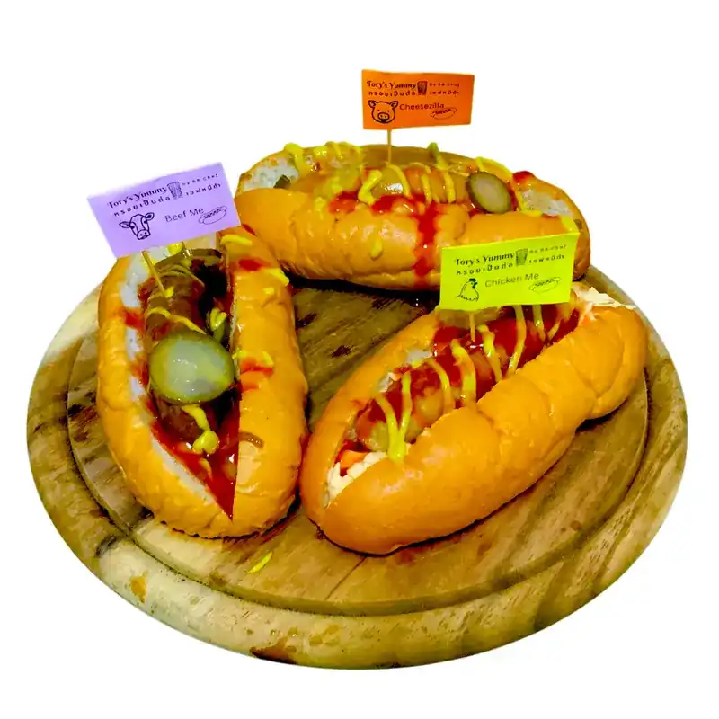 Three hot dogs on a wooden board, each with its own name flag