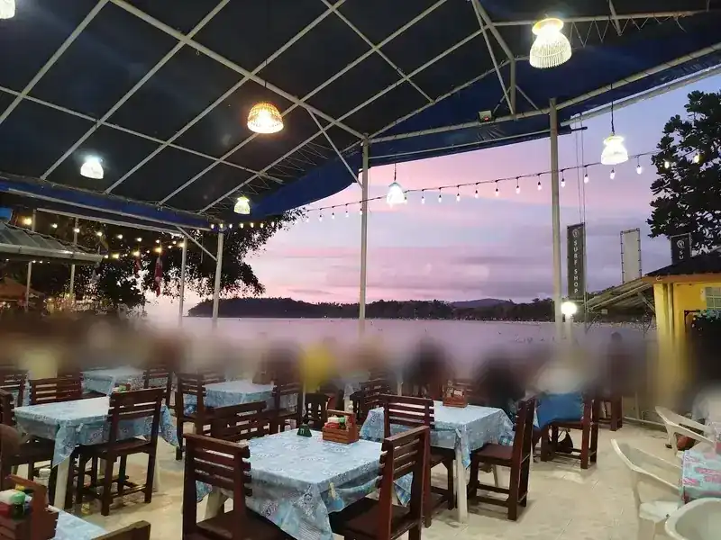 Tables under the blue roof at dusk, with the bay behind