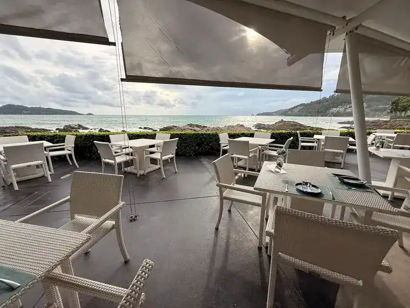 Covered terrace with white chairs, looking out over the sea