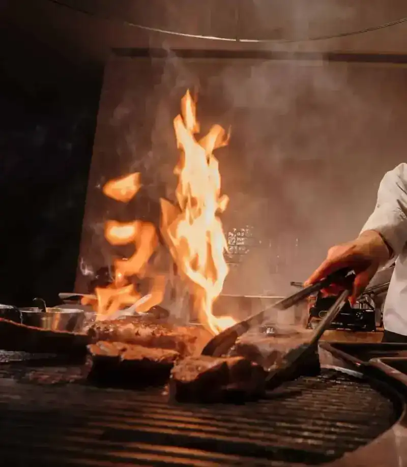 Flames over the grill as tongs turn the beef