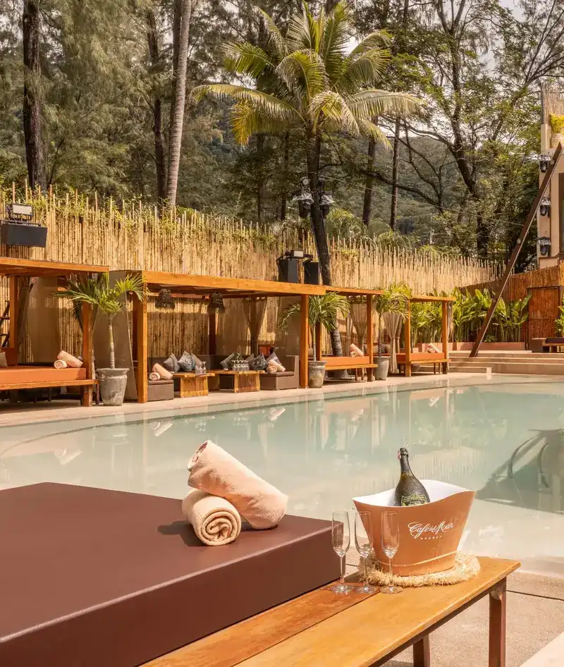 The pool at Café del Mar Phuket, lined with wooden cabanas, bamboo and palms