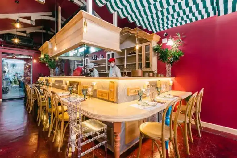 The chef's bar: a pale wooden counter with stools around an open kitchen, red walls and the striped canopy above