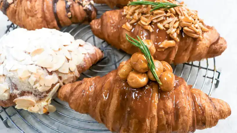Croissants on a wire rack, topped with caramel, almonds and macadamia nuts