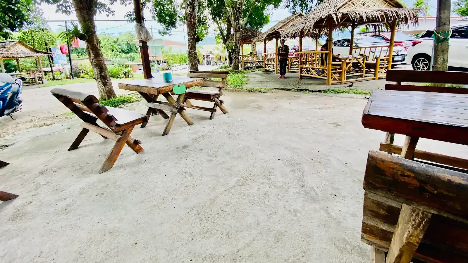 The garden at Isan Ban Hao: wooden tables on the yard and bamboo huts with thatched roofs under the trees