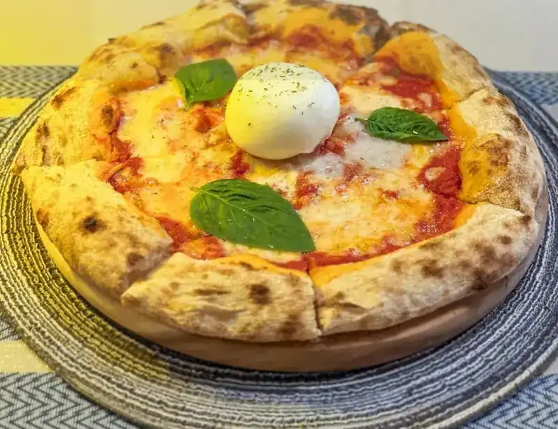 Pizza with tomato, melted cheese, basil leaves and a whole burrata in the middle