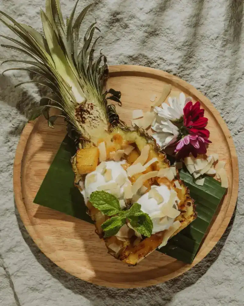 Half a grilled pineapple filled with coconut ice cream, toasted coconut and mint on a wooden board