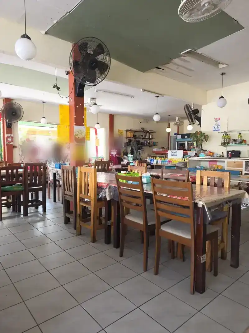 The dining room with wooden tables and chairs, fans on the walls and an open front