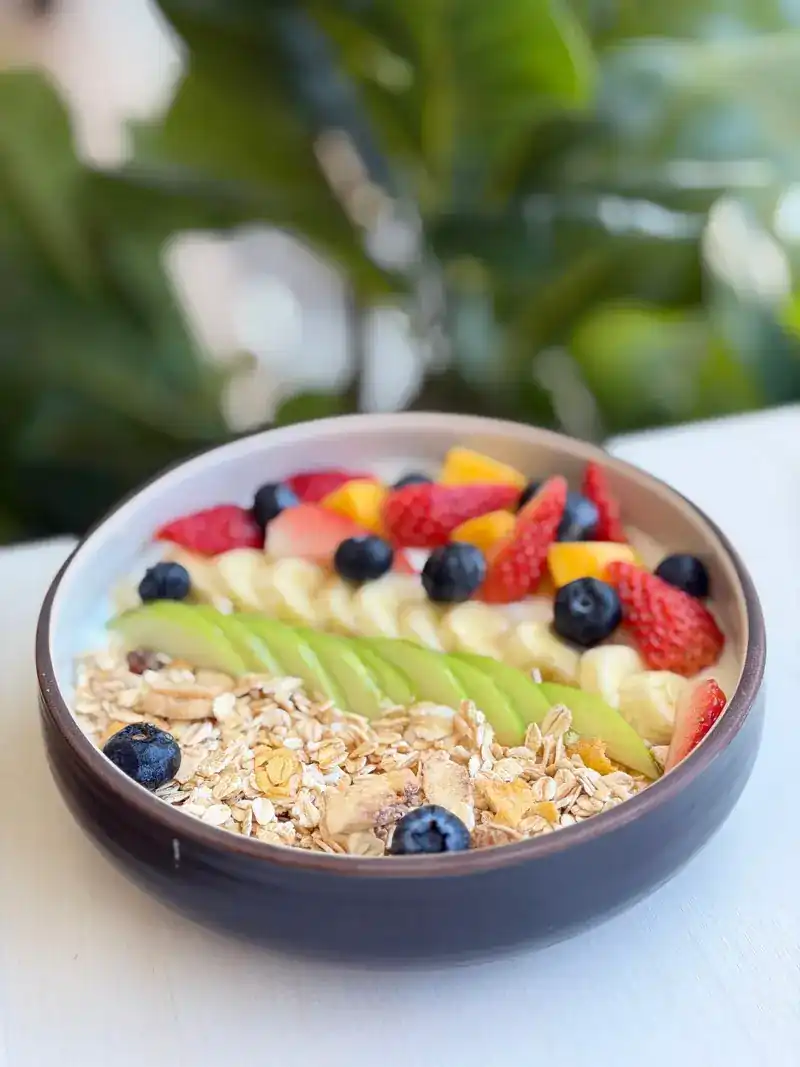 A muesli bowl topped with strawberries, blueberries, banana and other fresh fruit