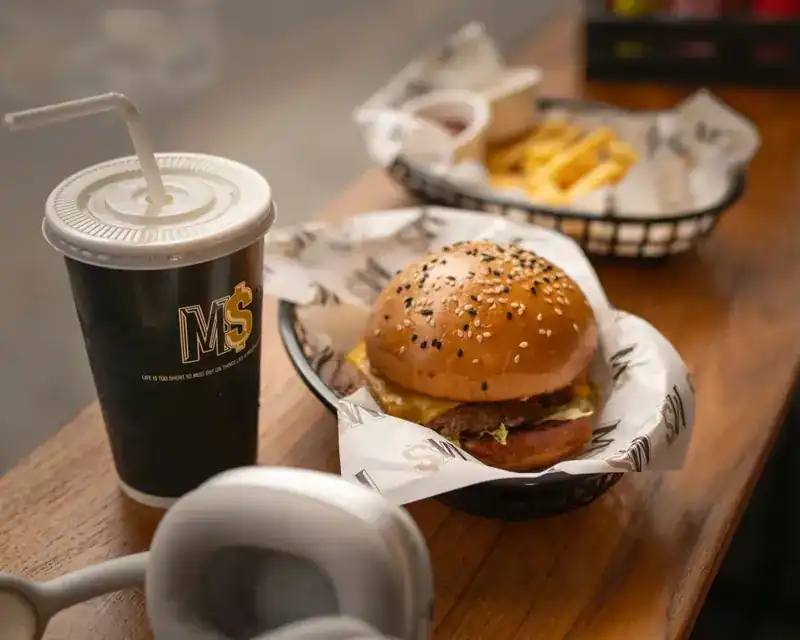 A burger in a basket on the wooden counter, with fries and a cold drink