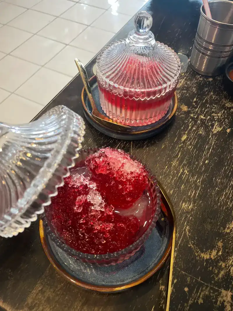 Two shaved-ice sweets with red syrup in cut-glass jars on a dark wooden table