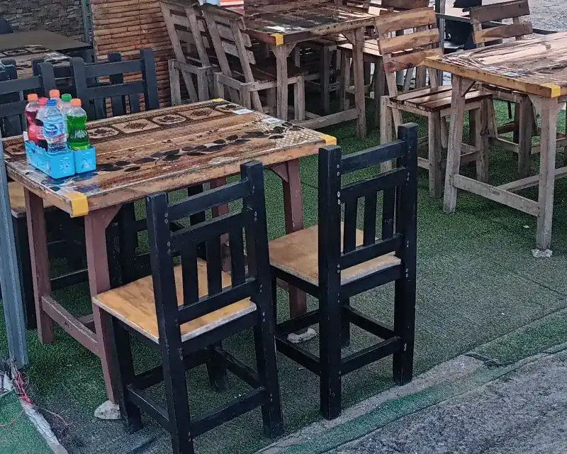 Wooden tables and chairs set out on green matting at the roadside