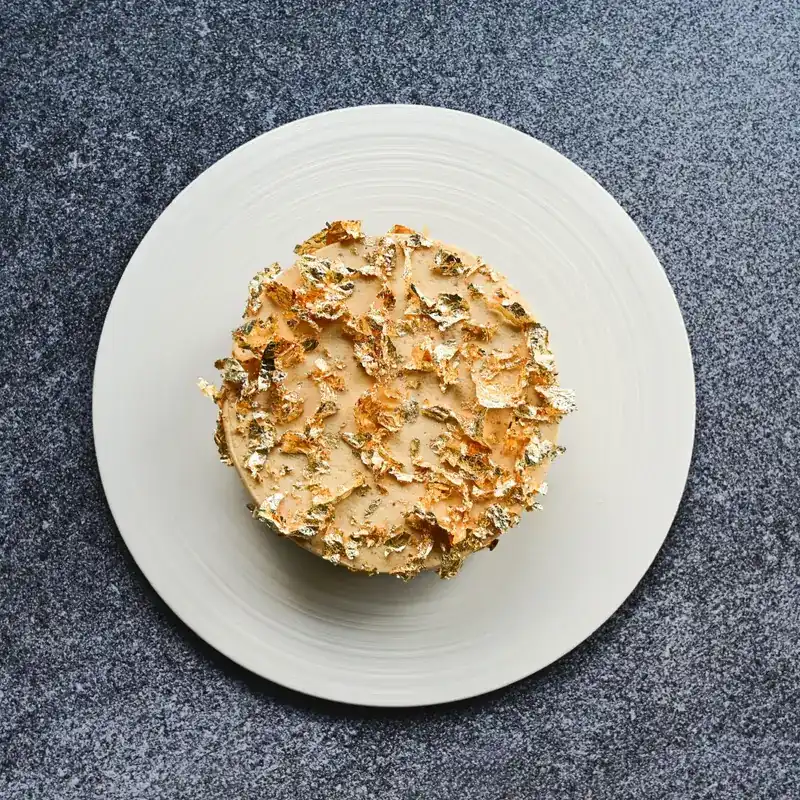 A round dish covered in gold leaf on a white plate, seen from above