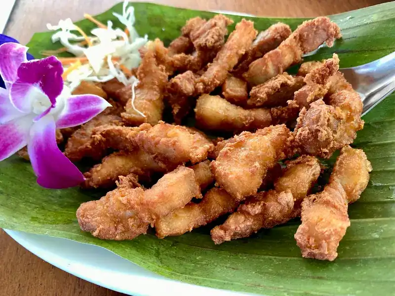 Golden fried strips on a banana leaf, with an orchid and shredded cabbage