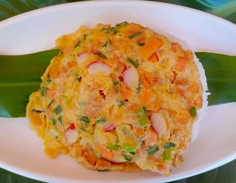 An omelette with crab stick, spring onion and carrot over rice