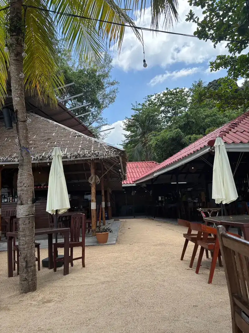 Thatched and red-roofed buildings with tables set out on the sand on a sunny day