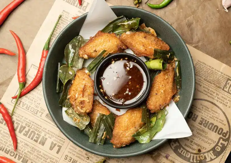 Fried chicken wings with pandan leaves around a bowl of chili dip
