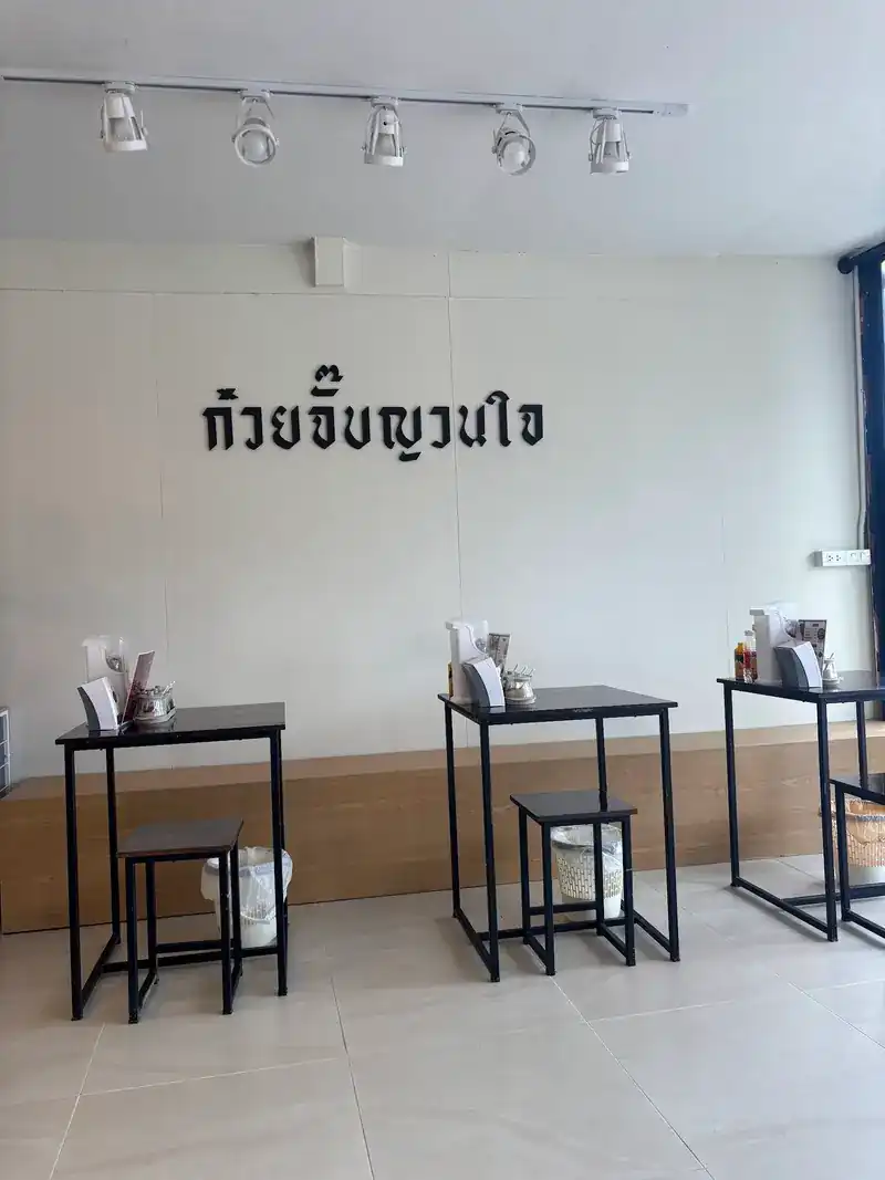 Inside the shop: the name on a white wall, black steel tables and stools, a wooden bench