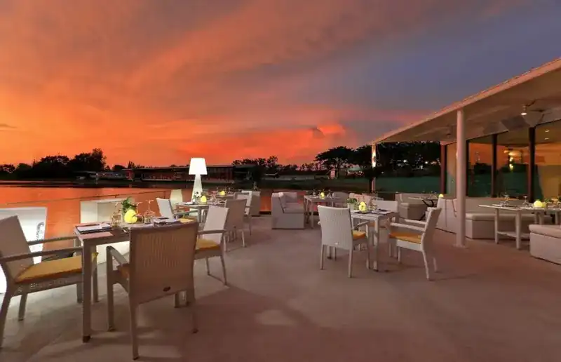 The terrace at dusk under an orange sky, lamps lit on the tables