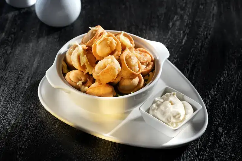 A bowl of golden fried dumplings with a dish of sour cream
