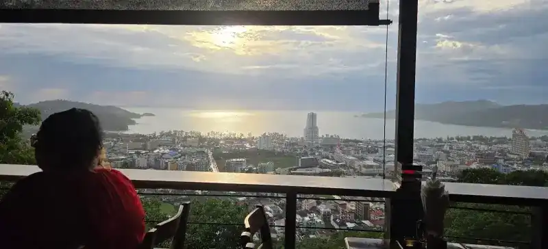 A guest seen from behind, looking past the railing at the sun over Patong Bay