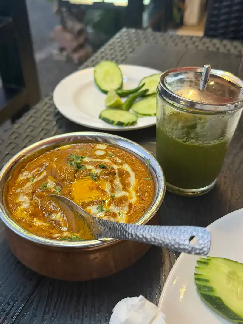 A curry in a copper bowl with cucumber and a green drink