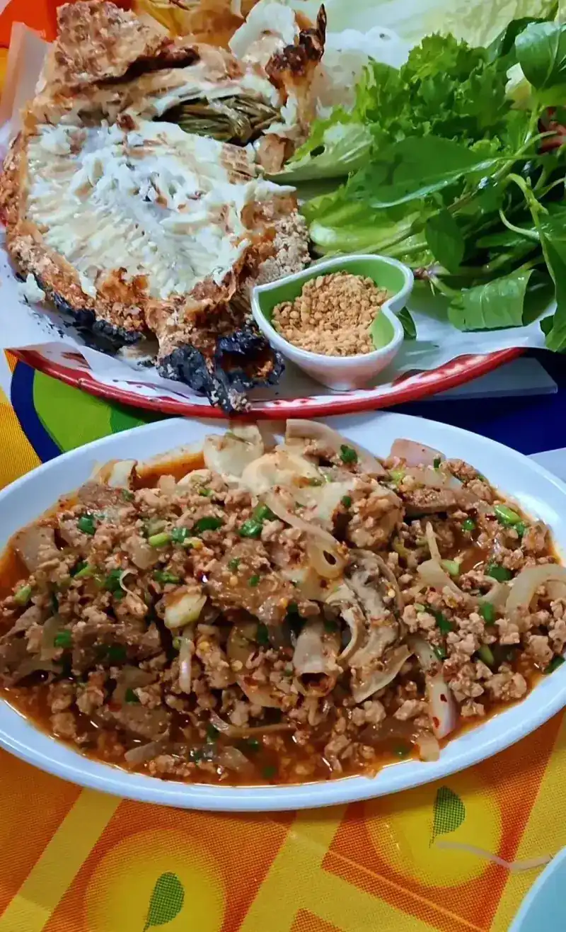 A plate of larb in front of a grilled fish with lettuce and fresh herbs