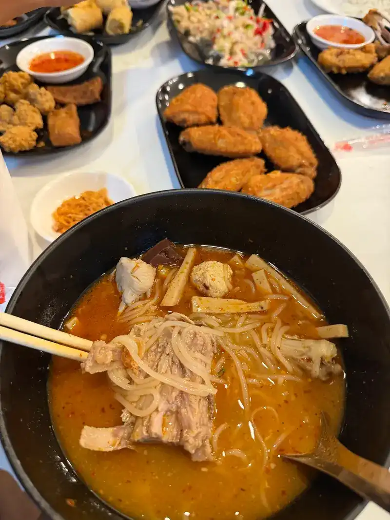 A noodle bowl with fried snacks and salads around it on the table