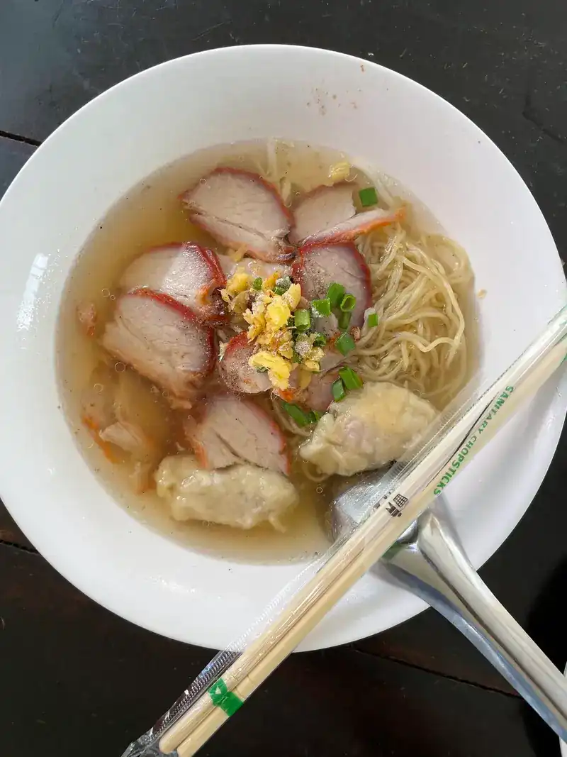 A bowl of egg noodle soup with red pork slices and wontons