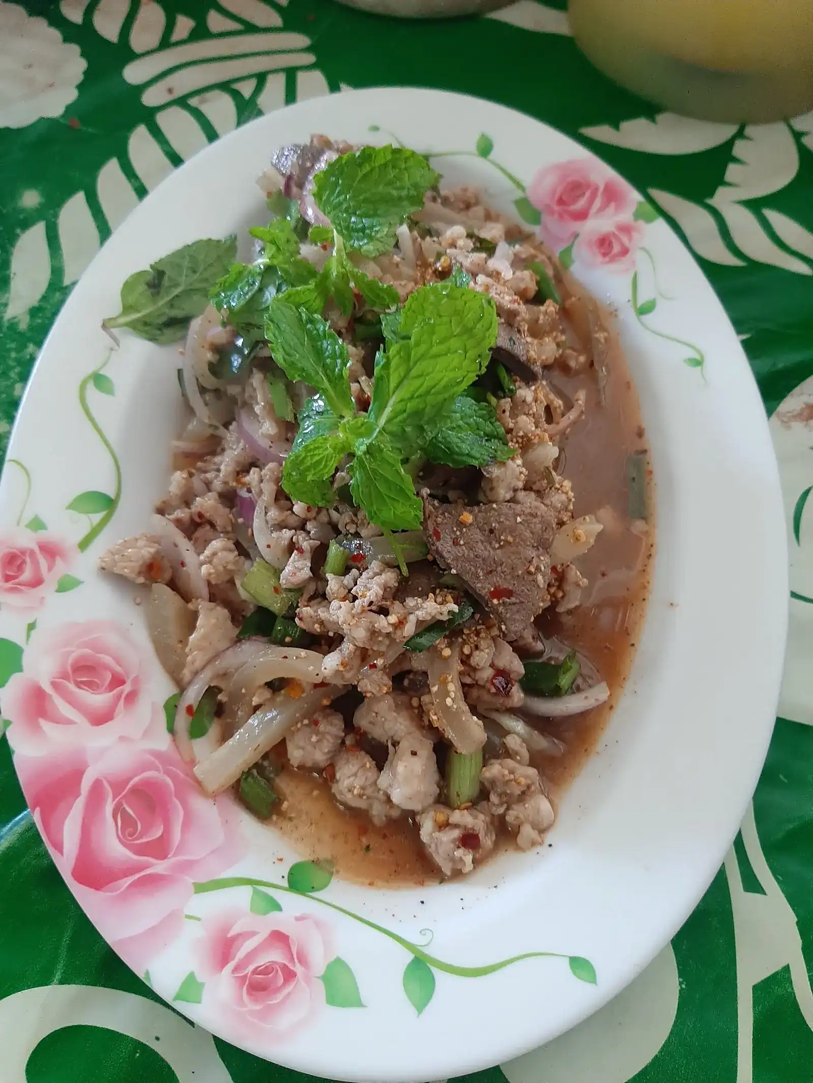 Laab with fresh mint and sliced liver on a rose-painted plate, on a green tablecloth