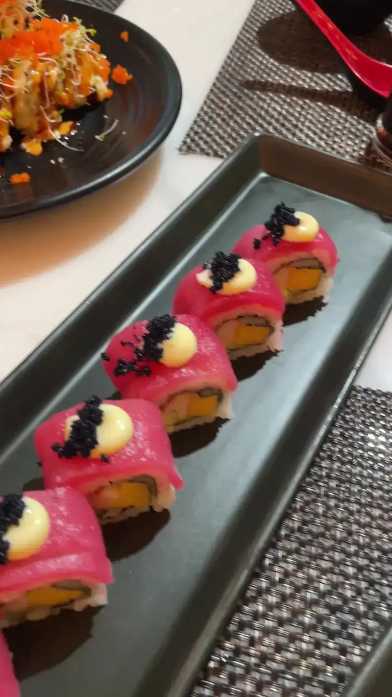 Tuna-wrapped sushi rolls with mayonnaise and black roe on a black plate