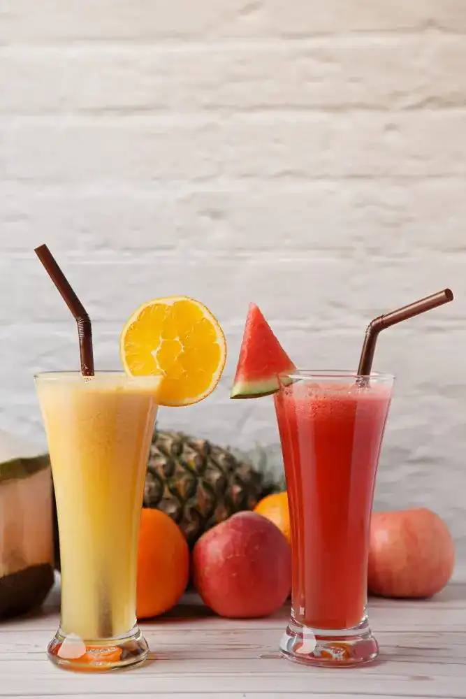 Two tall glasses of fruit juice with orange and watermelon slices