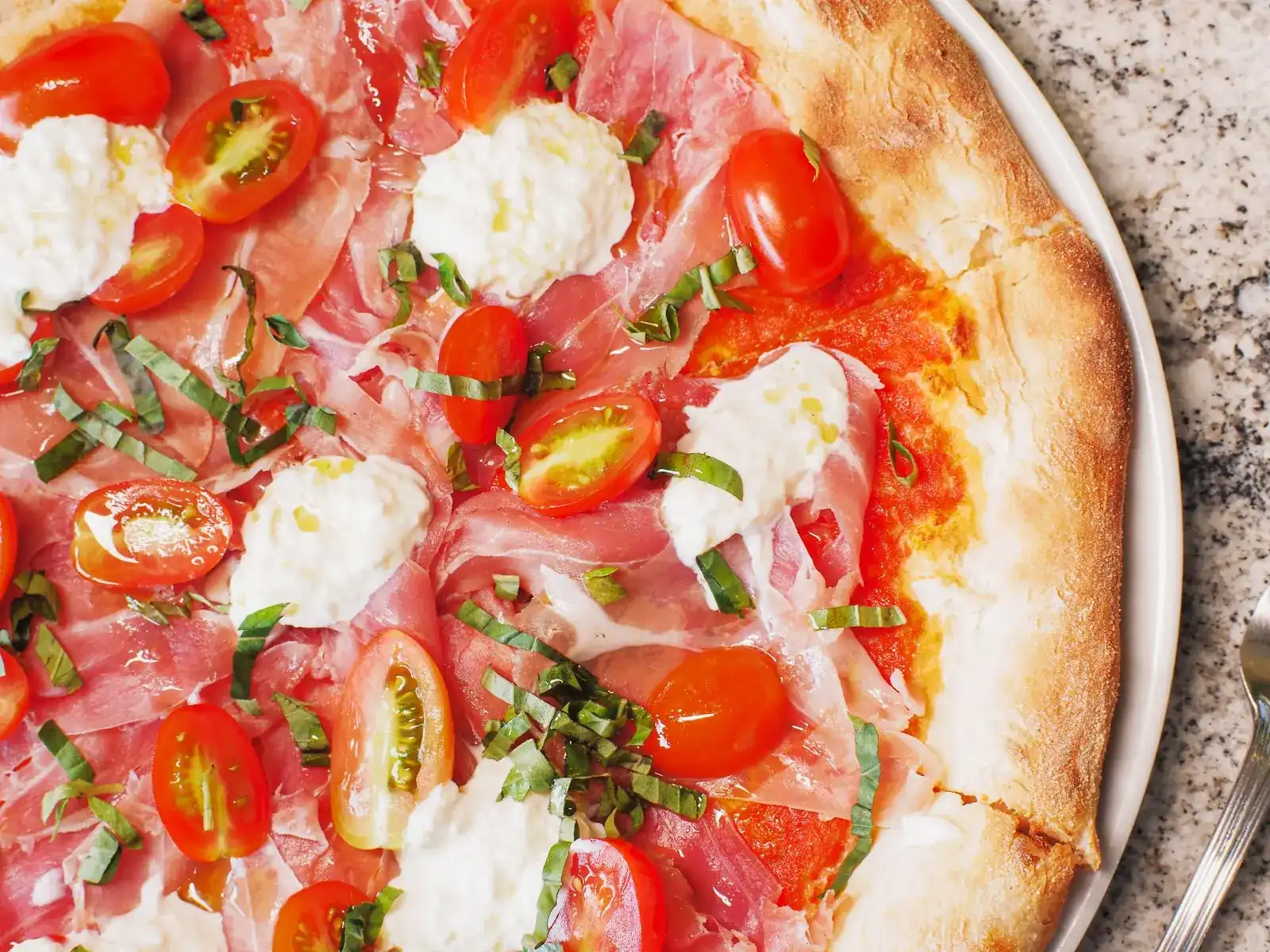Pizza topped with Parma ham, cherry tomatoes, basil and spoonfuls of soft fresh cheese