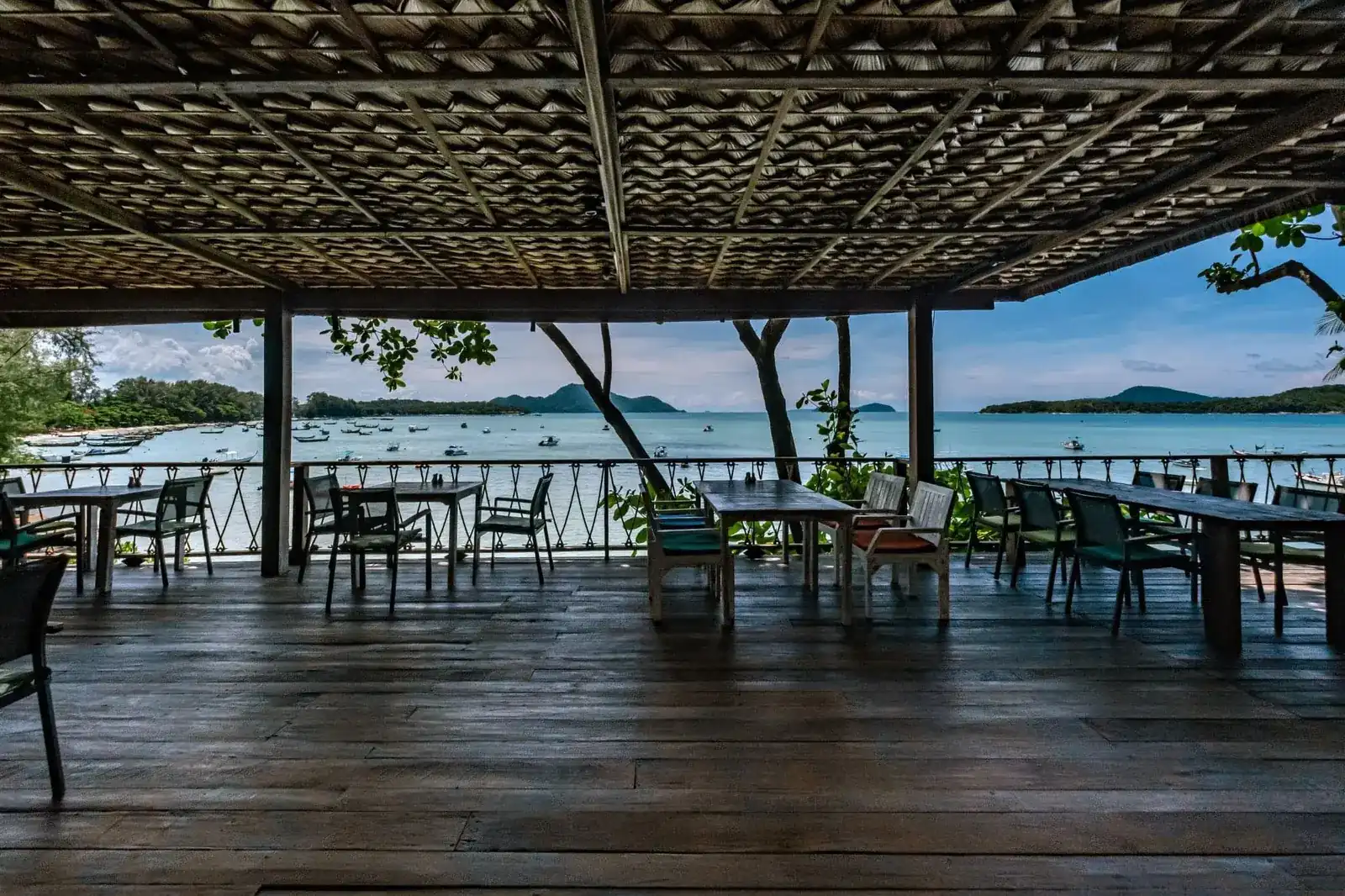 The open deck under a thatched roof, tables along the railing and Rawai bay beyond