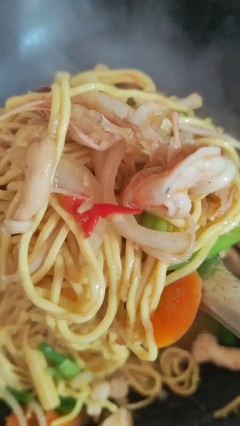 Yellow noodles with prawns, chilli and carrot being stir-fried in a steaming wok
