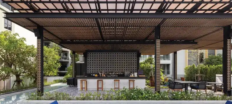 The bar under a timber pergola, with stools at the counter and a garden in front