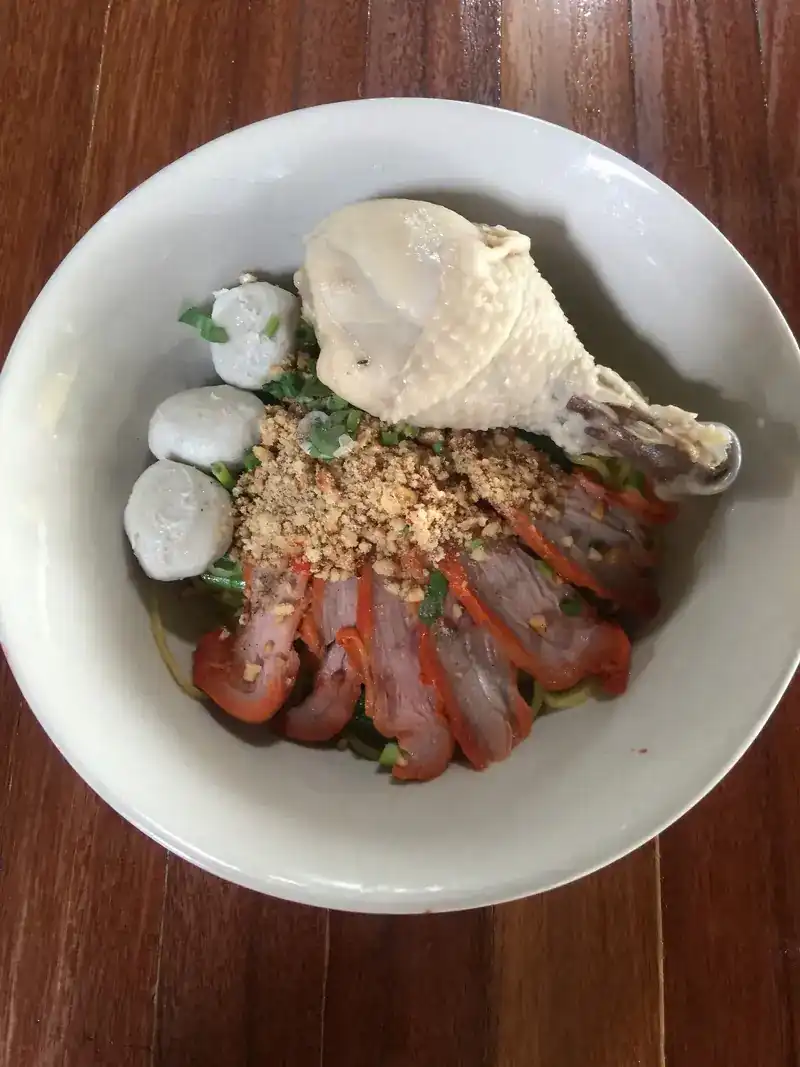 A bowl topped with a chicken drumstick, red pork, meatballs and crushed peanuts
