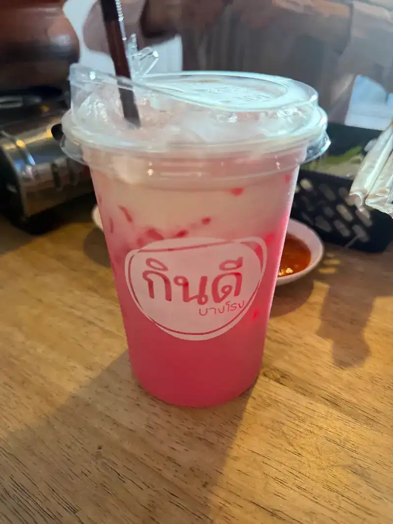 A pink iced milk drink in a cup printed with the กินดี บางโรง logo / เครื่องดื่มนมเย็นสีชมพูในแก้วที่พิมพ์โลโก้กินดี บางโรง