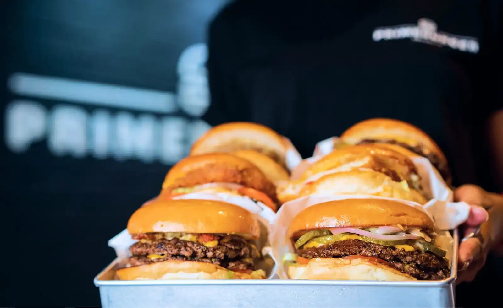 A steel tray stacked with smash burgers in paper wraps