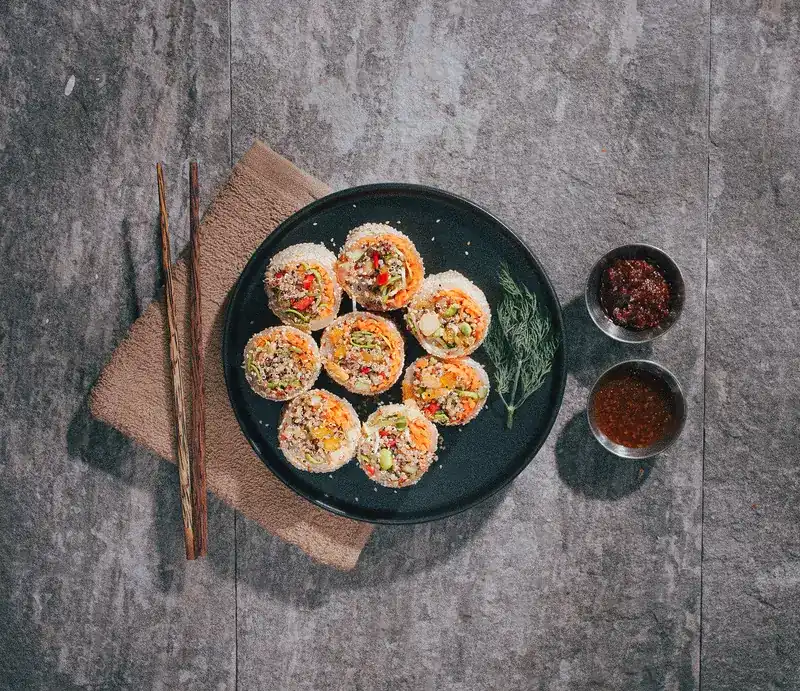 Fresh quinoa spring rolls on a black plate with two dipping sauces